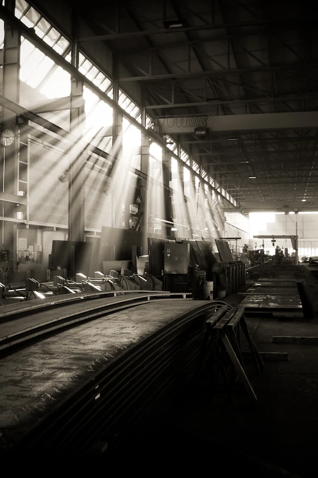 La lumière traverse les hautes fenêtres d’un atelier industriel.