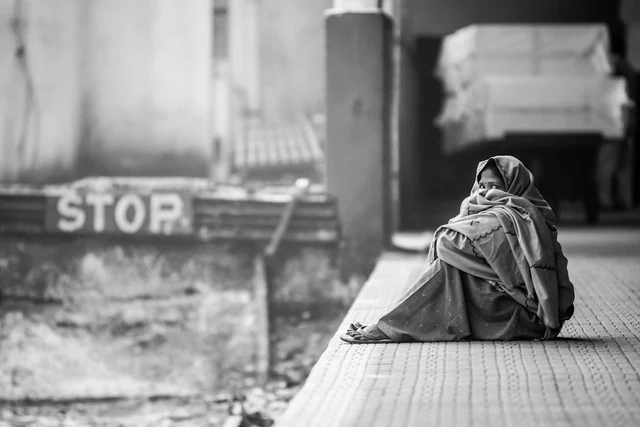 Une femme enveloppée dans un châle, assise sur un quai, en Inde.