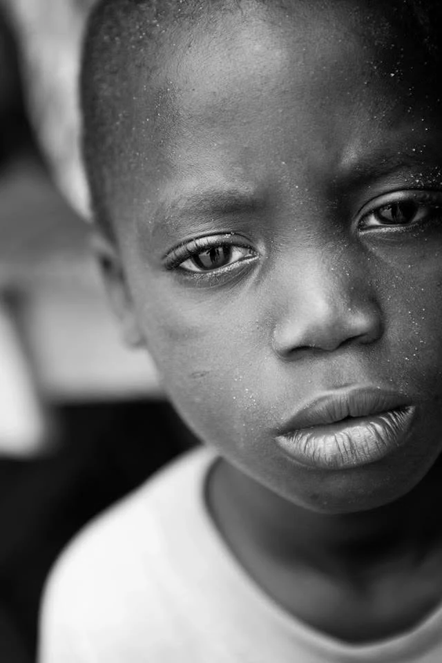 Portrait rapproché en noir et blanc d’un enfant au regard direct, la tête légèrement inclinée.